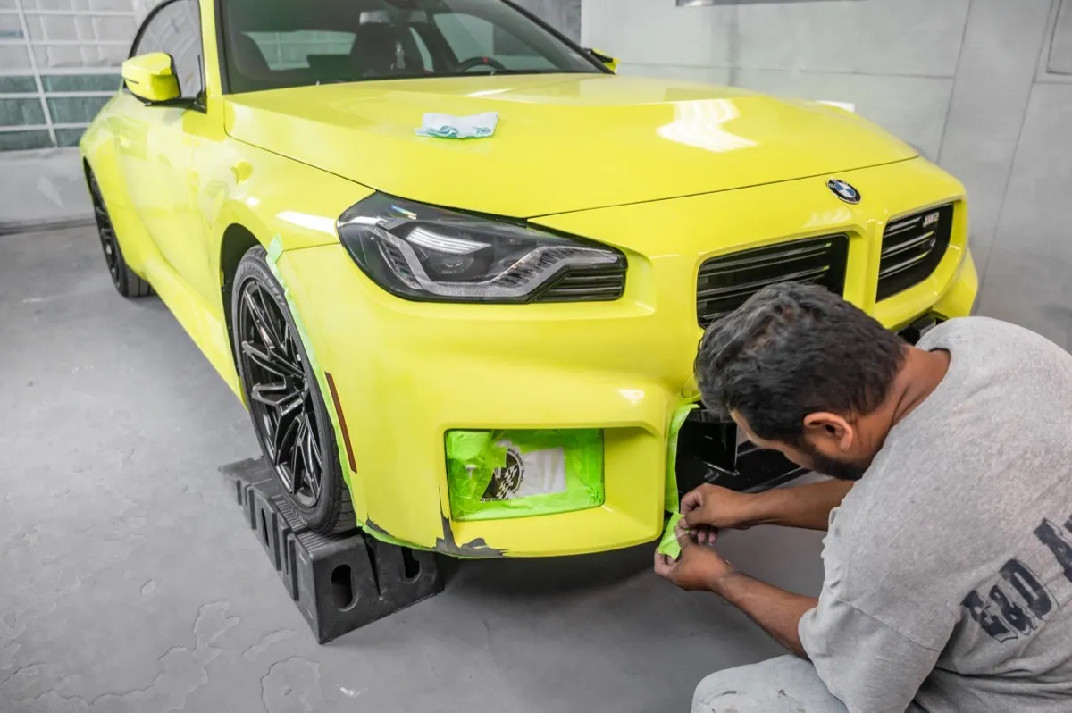 Technician masking a yellow BMW M2 bumper